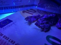 Small chunks of Thulium metal on top of a 10 Euro bill. One photo is under a daylight lamp, the other photo is under a black (UV) light. The Euro bill has small fluorescent fibers striped in red, green, and blue. Thulium may be responsible for the blue fluorescence, according to the Wikipedia article about Thulium. The Guatemalan bill behind the Thulium sample is not confirmed to be made with Thulium, even though it also has fluorescent fibers. It was placed behind the sample for decoration.