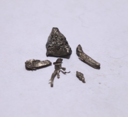 One chunk and four smaller chunks of shiny Ytterbium metal. The smaller chunks appear dendritic (hair-like).