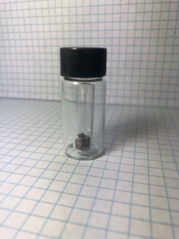 Small chunks of slightly oxidized Dysprosium metal in an ampoule, itself in a small bottle