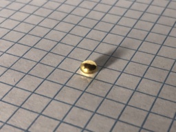 1 gram bead of Gold resting on grid paper