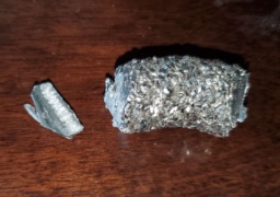 Two chunks of Zirconium metal: a small wedge-shaped chunk, and a larger bent-cylinder shaped chunk with a bumpy surface