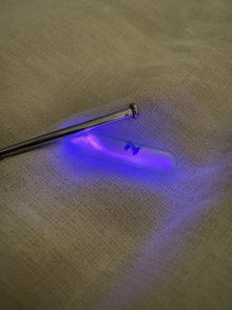 A sample of Nitrogen gas in an ampoule with a high voltage source next to it, causing the Nitrogen inside to emit a beautiful pink-purple glow.