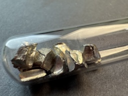 Shiny chunks of Cadmium metal in an ampoule, against black and white pieces of construction paper