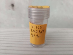 A sample of Gallium in a vial itself inside a bottle. Orange construction paper is fixed on the outer bottle with the symbol "Ga" and the electron shell.