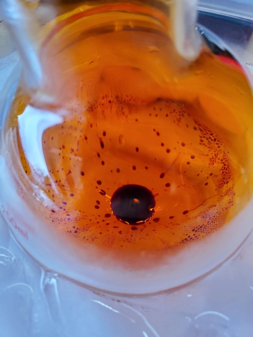 Bromine in a spherical beaker in an ice bath. Bright orange vapor fills the beaker.