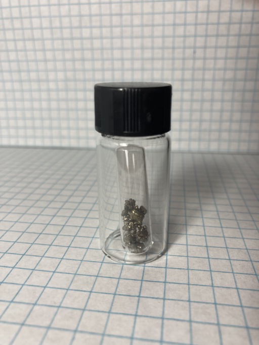 Small shiny piece of Europium metal, in an ampoule which itself is in a small bottle. Samples of this metal are usually found very dark and oxidized because Europium is an extremely reactive metal. This sample is shiny.