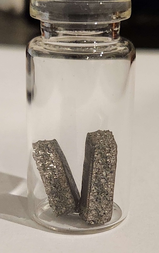 Two roughly rectangular chunks of Holmium metal. The side of the chunks show the internal poly-crystalline structure.