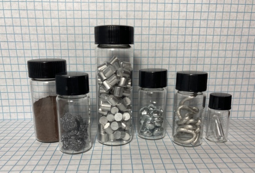 Boron group: amorphous brown |b| powder, dark crystalline |b|, a bottle of |al| slugs, |ga| pellets, thick |in| wire, and a small piece of |tl| metal