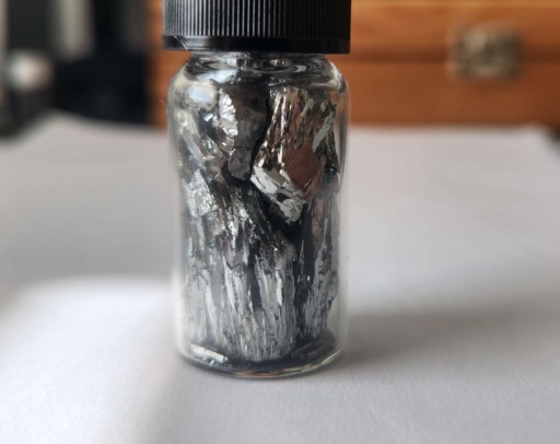 Tellurium can be commonly found in two allotropes (elemental forms): brittle silvery crystals, and amorphous (lack of a molecular structure) dark gray powder. The first photo is a bottle of small, dark gray, amorphous chunks, and the second photo is a bottle of brittle, shiny, silvery chunks.