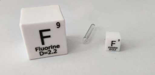 Two PTFE cubes: 1 inch cube on the left, and 1 cm cube on the right. PFTE is a long chain of |c| and Fluorine, and Fluorine makes up about 82.6% of the mass. In between the two cubes is an ampoule of 30% Fluorine and 70% |he|. Diluting the Fluorine helps it not destroy the container it’s in.