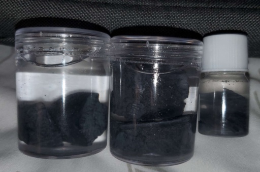 Three bottles filled with oil and multiple chunks of Lanthanum metal. Lanthanum is extremely difficult to keep shiny, even in oil. These samples have a heavy layer of black tarnish.