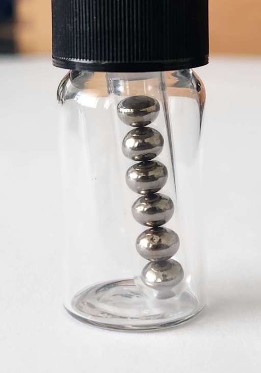 Six polished, extremely shiny beads of Hafnium metal in an ampoule, itself in a bottle. Polished samples of Hafnium are a rare sight.