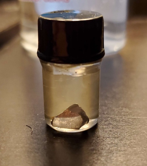 A small chunk of Thallium in a bottle under oil