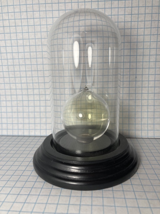 Chlorine gas inside a spherical ampoule, which in itself is inside a glass dome on a decorative black base plate. The faint yellow color of Chlorine is visible within the inner ampoule.