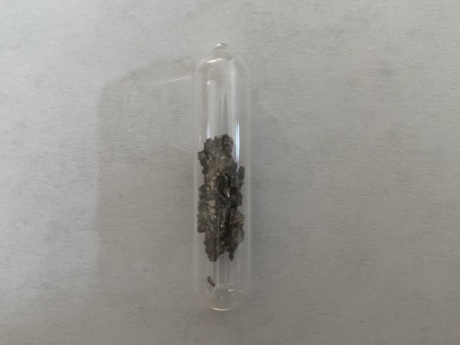 Small rough chunks of slightly oxidized, slightly brassy Calcium metal in an ampoule