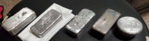 A collection of silvery ingots, from left to right: |sn|, |pb|, |zn|, |bi|, and |al|