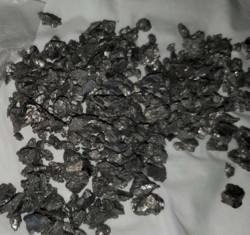 Many small pieces of dull gray Yttrium metal laid out on tissue paper