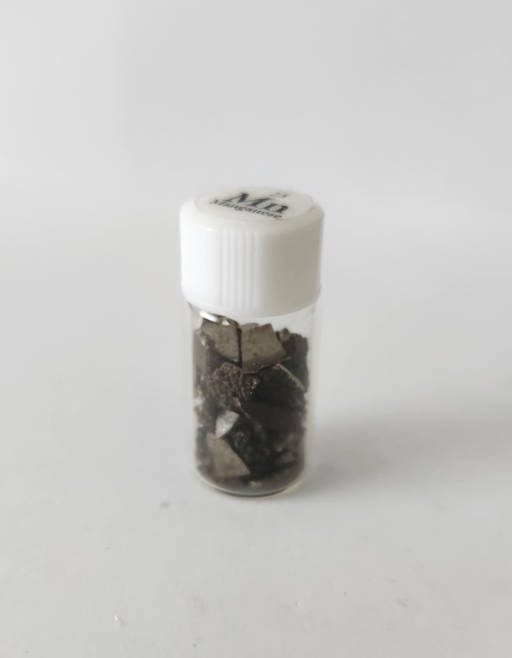 Moderately oxidized chips of Manganese metal with a very bumpy surface, in a small bottle with lid