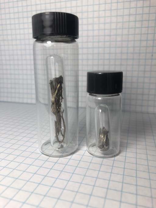 Two ampoules of Samarium metal. The larger ampoule has a larger dendritic (hair-like) piece, and the smaller has a small chunk of this metal.