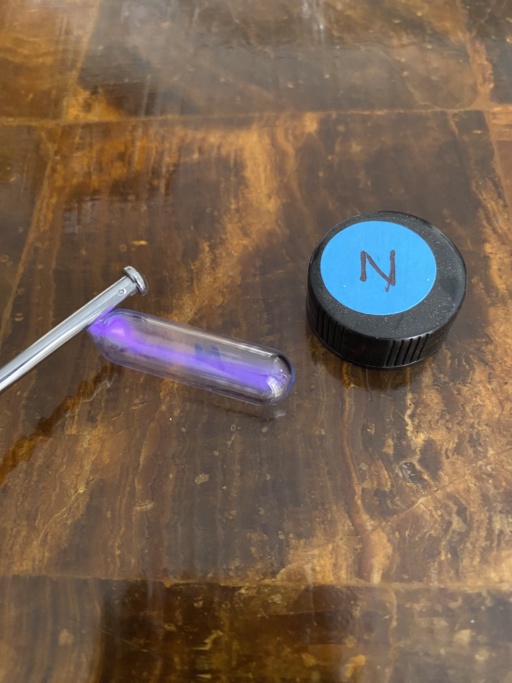 A sample of Nitrogen gas in an ampoule with a high voltage source next to it, causing the Nitrogen inside to emit a beautiful pink-purple glow.