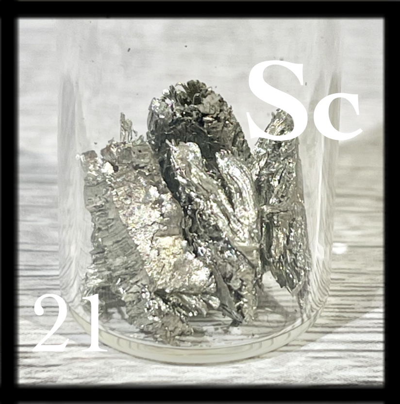 Small, shiny, slightly brassy chunks of Scandium metal in a bottle